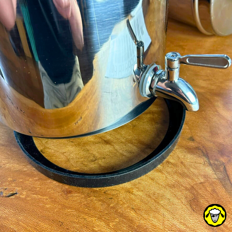 Vue rapprochée d'un robinet en inox fixé sur une cuve de filtre à eau, détail de la base caoutchouc sur un plan de travail en bois.