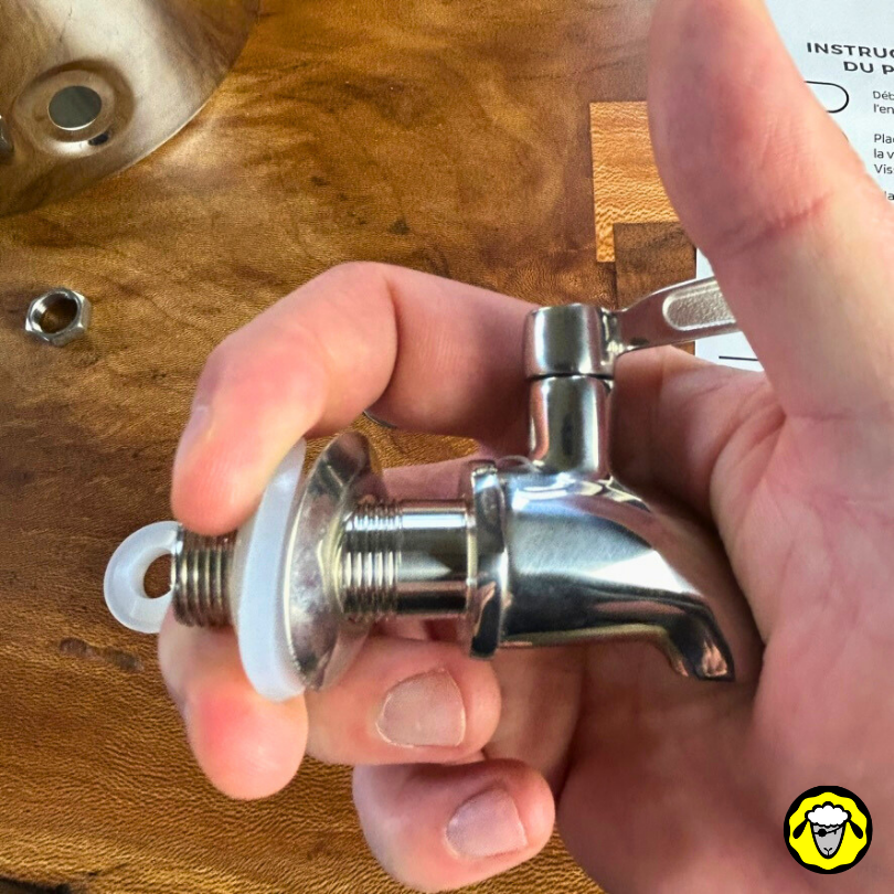 Mains tenant un robinet de filtre à eau en inox avec ses composants de montage avant installation (rondelles et joints caoutchoucs).