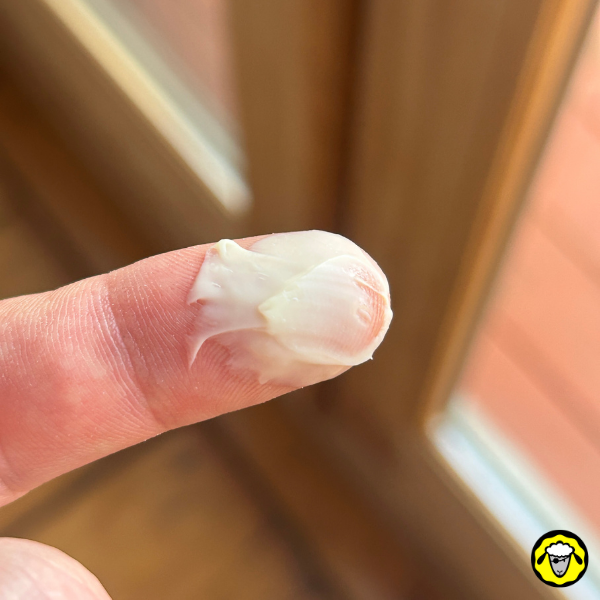 Une petite quantité de crème blanche posée sur un doigt. La texture semble onctueuse, indiquant une utilisation potentielle comme baume ou crème hydratante.