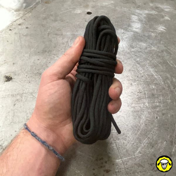 Une corde en paracorde noire soigneusement enroulée et tenue dans une main. La corde semble robuste et polyvalente, idéale pour des usages en extérieur ou survivalistes, comme une corde à linge ou pour monter un abri.