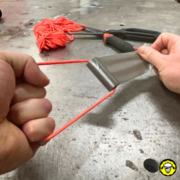 Deux mains en action déroulant le duct tape fixé sur une paracorde orange, avec des ciseaux et des fournitures en arrière-plan.
