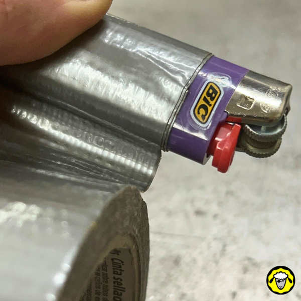 Gros plan sur un briquet violet avec plusieurs couches de ruban adhésif gris enroulé autour de lui, indiquant une méthode pour le transporter.