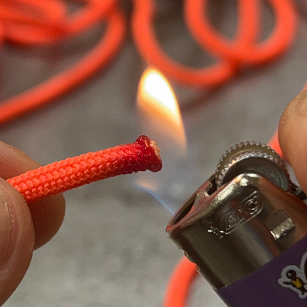 Extrémité fondue d’une paracorde orange sous la flamme d’un briquet.