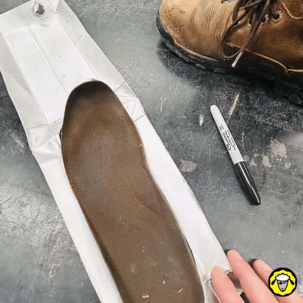 Une semelle existante posée sur la brique de bouillon aplatie, avec un marqueur utilisé pour tracer le contour en vue de découper une semelle personnalisée.