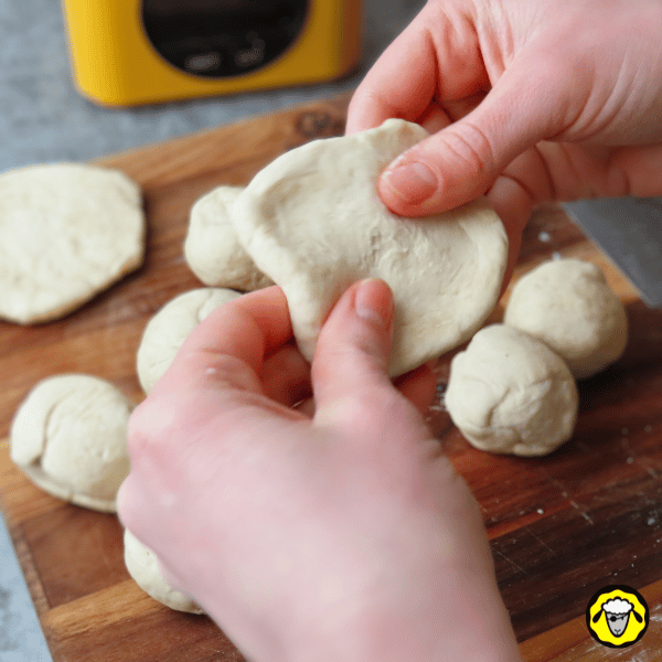 pain-maison-facile-cuit-a-la-poele-7 Une main aplatie une boule de pâte pour lui donner une forme de petit disque, préparant les pains à la cuisson.