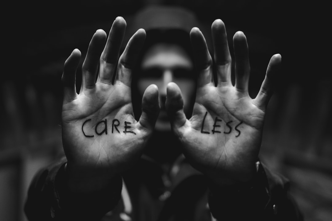 Photo by Mitchel Lensink gray scale photography of man raising both hands with care less text on palm
