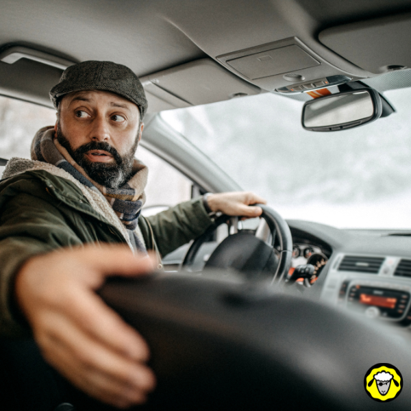 Conducteur barbu effectuant une marche arrière manuelle dans un véhicule en hiver, regard vigilant vers l’arrière. Scène typique de conduite en conditions difficiles sans aide électronique, soulignant la nécessité d’une autonomie complète et d’un entraînement pratique pour manœuvrer en situation de survie ou de black-out.