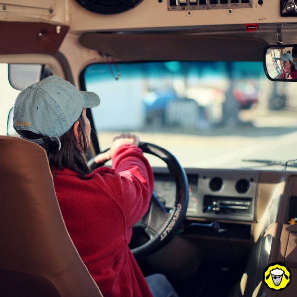 Femme au volant d’un fourgon ancien, concentrée sur sa conduite, sans technologie d’assistance moderne. Image d’un mode de transport résilient, adapté aux survivalistes ou aux familles autonomes cherchant à s’éloigner des dépendances numériques.