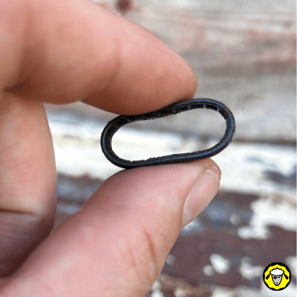 Alliance tactique en silicone noire, compressée entre deux doigts, montrant sa flexibilité et sa résistance. Conçue pour les environnements hostiles, les activités outdoor et les situations survivalistes.