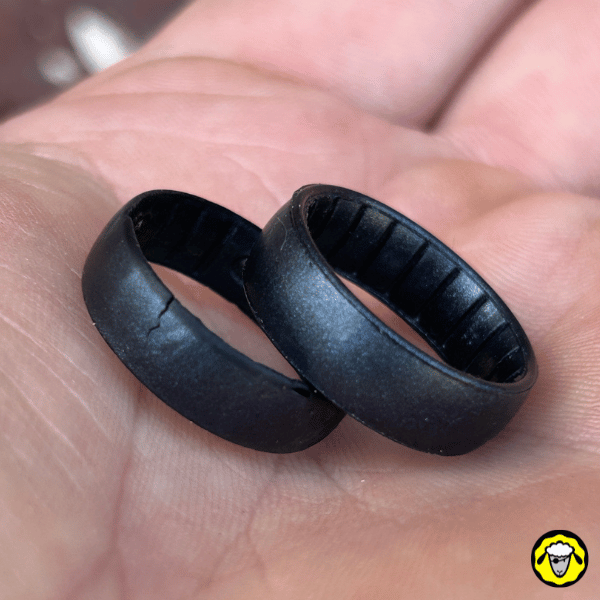 Deux alliances en silicone noires posées dans une main, dont une fissurée. Anneaux tactiques low-profile, pensés pour les survivalistes et métiers à risque, plus sûrs que les bagues métalliques.