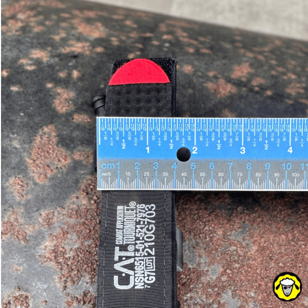 Gros plan sur l’extrémité rouge du garrot tourniquet CAT, placé sous une règle graduée pour illustrer la largeur de 4 centimètres du garrot.