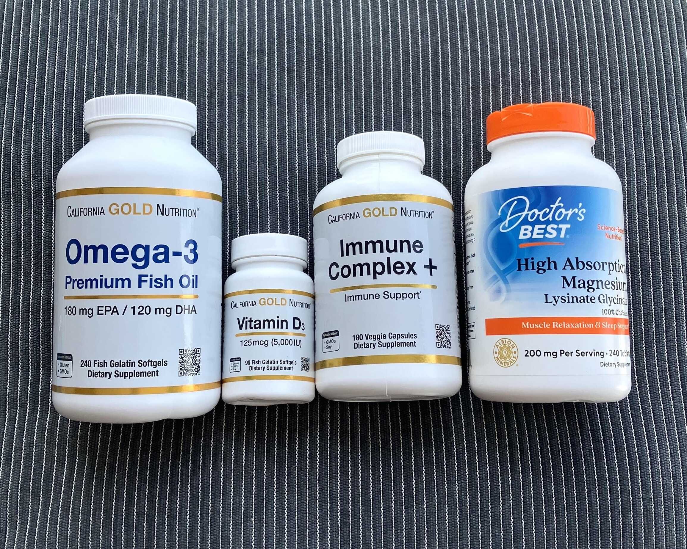 supplements-california-gold-magnesium-vitamine-d3 Quatre compléments alimentaires sur tissu rayé : huile de poisson oméga-3, vitamine D3, complexe immunitaire et magnésium à haute absorption.