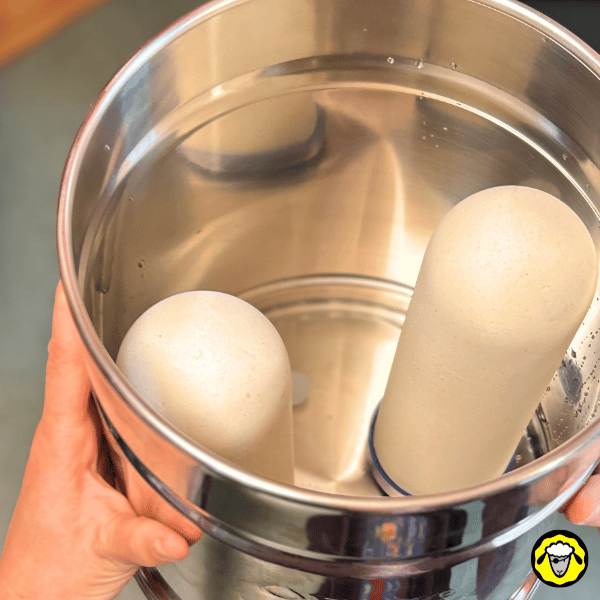 Réservoir supérieur d’un filtre à gravité Pure-Filters contenant deux cartouches céramique FTO+ immergées dans l’eau, première étape de la procédure de mise en pause avant un départ prolongé.