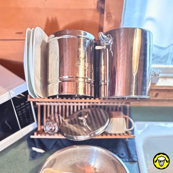 Filtre-A-Gravite-Vacances-FTO-10 Réservoirs en acier inoxydable d’un filtre à gravité Pure-Filters soigneusement nettoyés et séchés à l’air libre sur un égouttoir, étape finale de la préparation du système avant un départ en vacances.