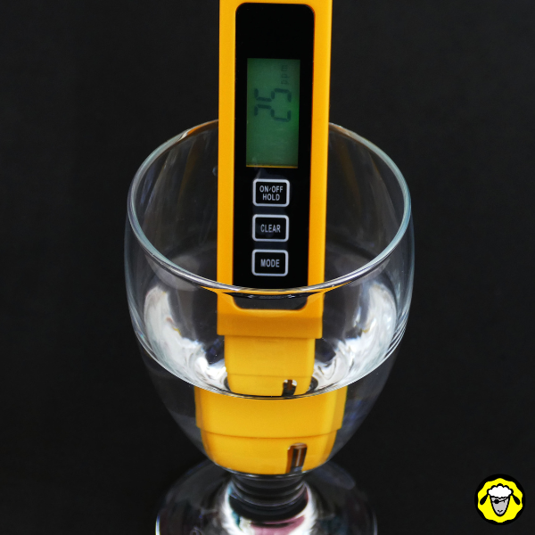 Appareil TDS jaune affichant 25 ppm, plongé dans un verre d’eau claire sur fond noir.