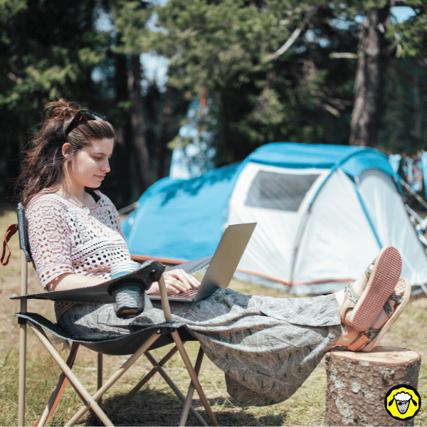 Femme installée en camping devant une tente, travaillant sur son ordinateur grâce à une connexion internet nomade adaptée au plein air.