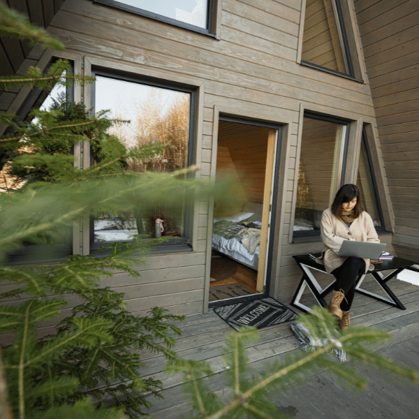 Femme installée devant un chalet en bois OFF GRID, travaillant sur son ordinateur tout en profitant d’un environnement naturel calme et connecté.