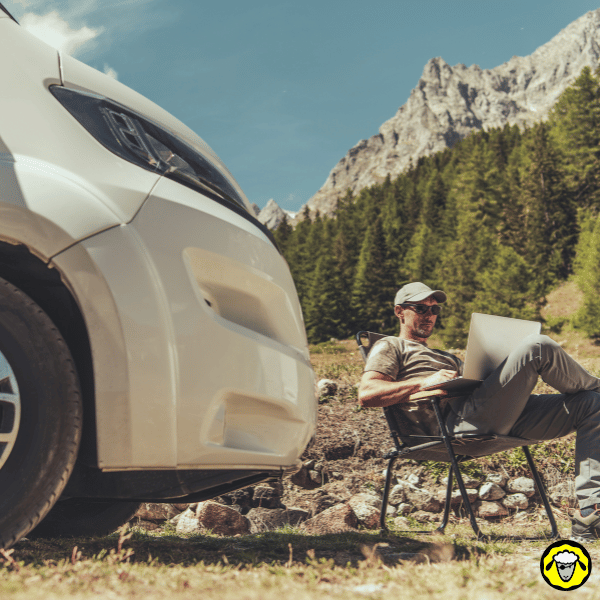 Homme assis devant son van en montagne, travaillant sur son ordinateur portable grâce à une connexion internet satellite adaptée au mode de vie nomade.
