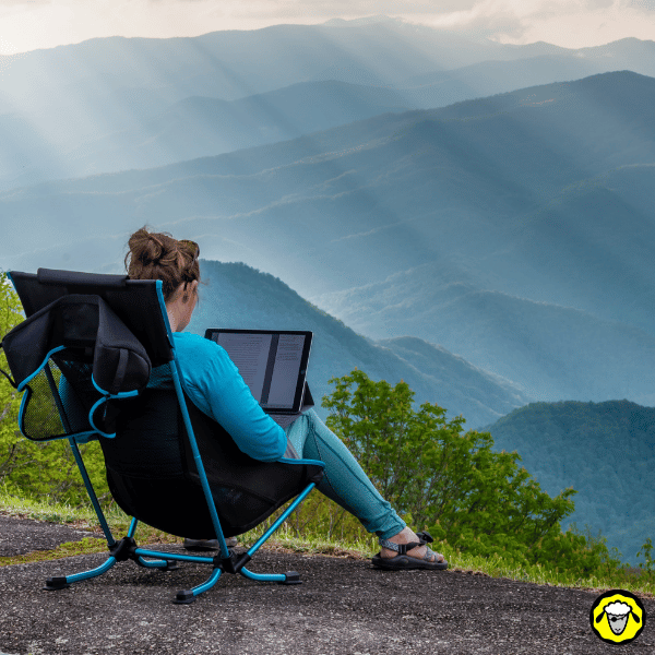 Personne travaillant sur son ordinateur face à une chaîne de montagnes, illustrant le télétravail en pleine nature avec une connexion internet nomade.