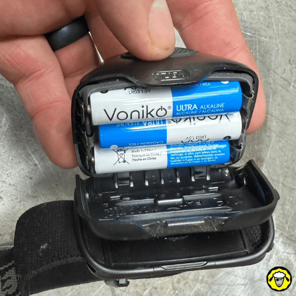 Compartiment batterie d’une lampe frontale à piles AAA, avec trois piles alcalines visibles.