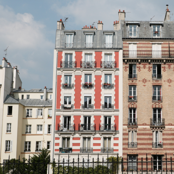Façades d'immeubles parisiens avec balcons et toits en zinc derrière une grille noire