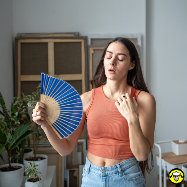 Femme utilisant un éventail pour se rafraîchir Une femme tient un éventail bleu et se rafraîchit dans une pièce, les yeux fermés.