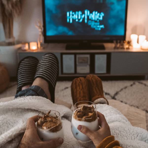 netflix-confort-tele-pantoufle Couple installé confortablement devant la télévision avec plaids et desserts, illustrant le confort moderne et la dépendance aux habitudes du quotidien.