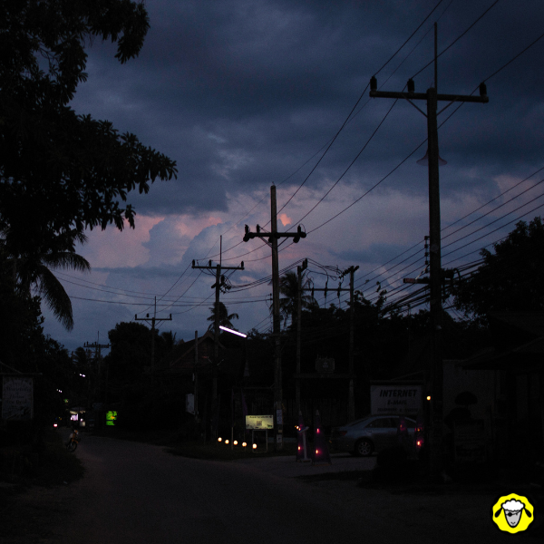 Rue plongée dans l’obscurité lors d’une panne de courant, avec des lignes électriques visibles sous un ciel d’orage.