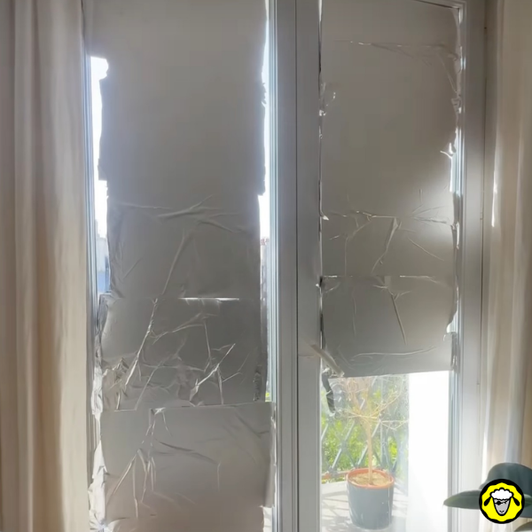 Papier aluminium collé sur des vitres de fenêtre pour limiter la chaleur dans un logement