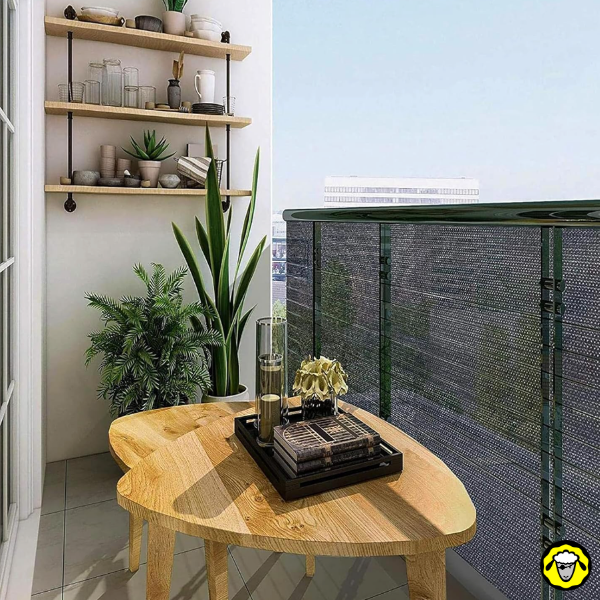 Balcon avec voile d’ombrage sur la balustrade, plantes et table en bois au soleil