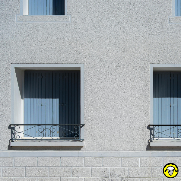 Facade d immeuble avec volets fermes et balcons, fenetres a l ombre